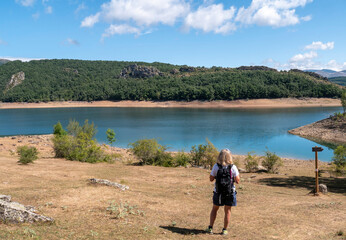 A Caucasian female hiker with blonde hair and sunglasses enjoying the beautiful view of a calm lake on a hot summer day