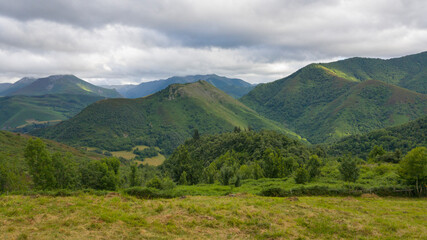 Obraz na płótnie Canvas Preciosas vistas bajo las grises nubes a las verdes montañas salpicadas por los rayos del sol donde se refugia el bosque de Muniellos en Asturias, España.