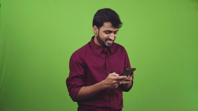 Asian man clad in burgundy colored shirt smiling and texting in a green screen shoot.