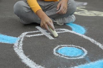 Child drawing rocket with chalk on asphalt, closeup