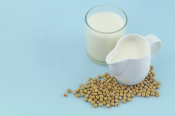 Soy milk in jug and glass and soy beans on blue background with copy space for text