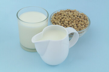 Soy milk in jug and glass with soy beans on blue background	
