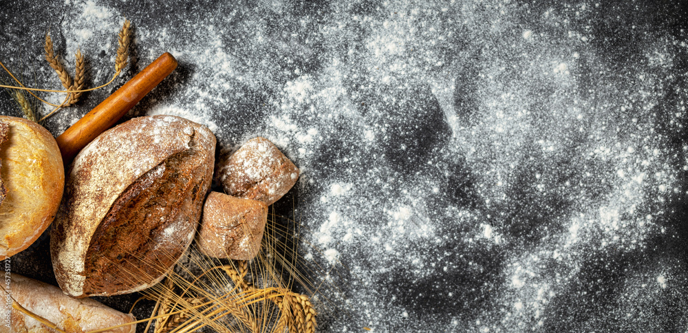 Poster bakery. freshly baked crispy bread and buns with ears of wheat on a dark background with copy space 