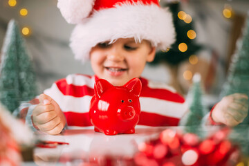 Young child in a Santa hat keeps a piggy Bank and sits in the kitchen with a decor for Christmas. Holidays, Traditions, baby food and health concept.