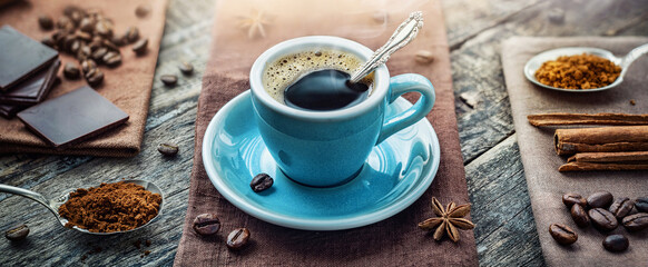 A cup of aromatic black coffee, a coffee maker, coffee beans of different varieties on the table. Morning espresso or Americano coffee for breakfast in a beautiful brown cup.