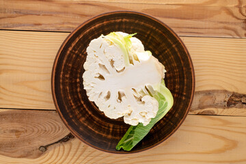 One half of fragrant organic cauliflower with a clay dish on a wooden table, close-up, top view.