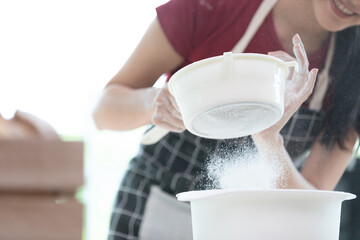 young woman housewife sifting flour from sieve in the kitchen