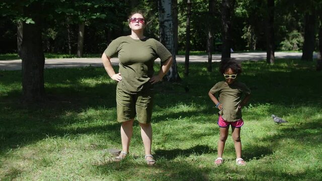 Mixed family - white woman and her black daughter doing simple warming up exercises in the park