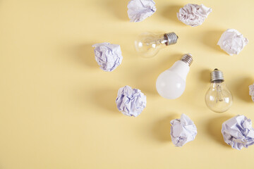 Creativity inspiration. Light bulbs and crumpled paper balls on yellow background.