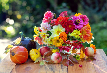 Autumn concept. A bouquet of beautiful flowers in a vase, pumpkins and apples in colorful leaves. autumn still life