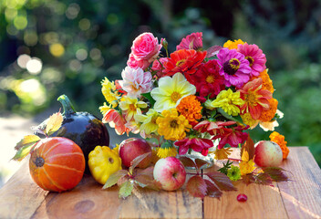 Autumn concept. A bouquet of beautiful flowers in a vase, pumpkins and apples in colorful leaves....