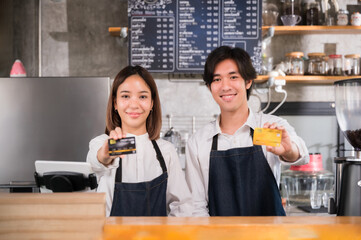 Couple Asian barista wear apron standing and smile holding show credit card with look at camera in counter at coffee shop.