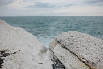 Seascape of white rocky coastline with water of green color bumping of its edge causing splatter, heavy grey clouds on horizon. Nobody around. Quiet place far from big city life. Power of nature