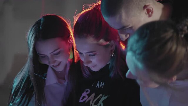 Group of teenagers watching footage of them roller skating on camera. Girl holding video camera in hands checking recording of friends doing tricks and pulling dance moves. Concept of youth, nightlife