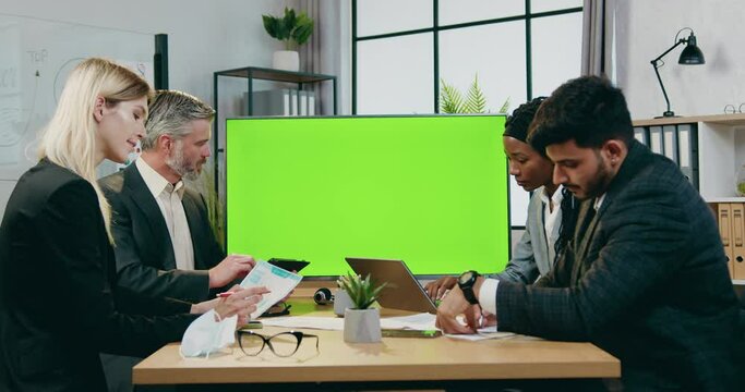Attractive confident successful experienced multiracial male and female business partners working together in modern boardroom near green chroma screen