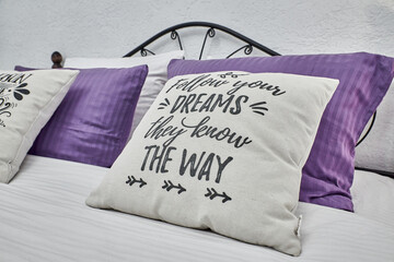 Light pillow with an inscription. Purple pillow. Pillows on a light bed. Black bed in a bright room. Coziness and warmth