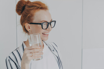Thirsty woman with red hair combed in bun drinks still water prevents dehydration holds glass