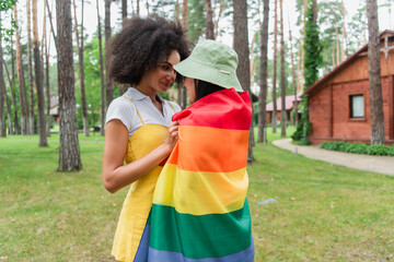 Smiling african american woman hugging girlfriend in lgbt flag outdoors.