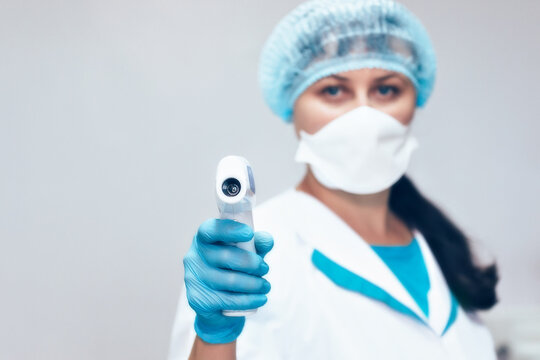 Measurement of body temperature with a non-contact thermometer. A woman doctor holds a modern infrared thermometer in her hand. Covid 19 incidence control.