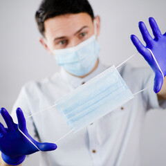 The masked guy holds out another mask. Doctor in a medical mask and gloves. The young man offers a protective mask. Portrait of a doctor on a white background.