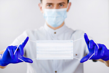 The masked guy holds out another mask. Doctor in a medical mask and gloves. The young man offers a protective mask. Portrait of a doctor on a white background.