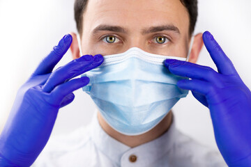 Handsome guy in a protective mask and gloves. The doctor adjusts the medical mask. Protection during quarantine. White background.