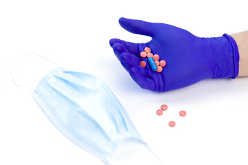 Pills in hand on a white background. Hand in a protective glove. Hand in a medical glove. Protective mask on the table. Virus protection. Medicines in hand. Vitamins to strengthen the immune system.