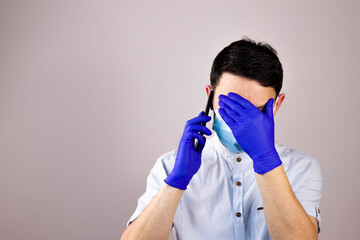 The doctor is talking on the phone in a protective mask and gloves. The guy got the bad news over the phone. The guy speaks on the phone and covers his face with his hand. Pandemic.