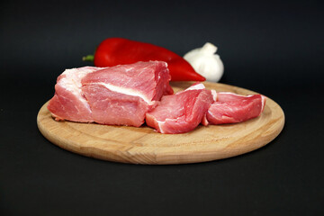 pork meat, red pepper, garlic on a round wooden board on a black background