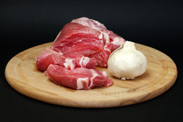 pork meat and garlic on a round wooden board on a black background