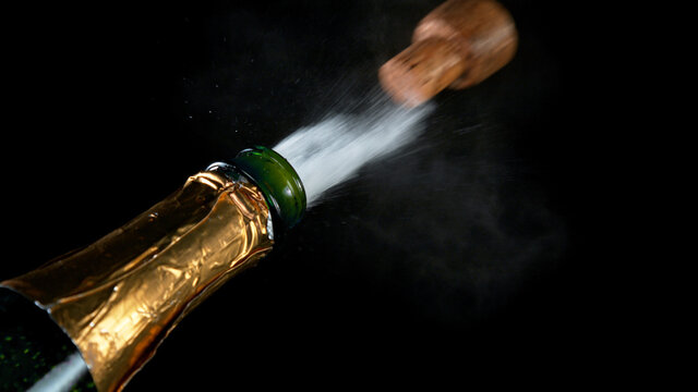 Freeze motion of Champagne explosion with flying cork closure, opening champagne bottle closeup isolated on black background.