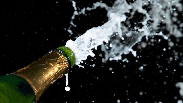 Freeze motion of Champagne explosion with flying cork closure, opening champagne bottle closeup isolated on black background.