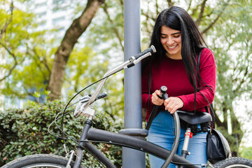 Young latin woman locking her bicycle in a post in the park