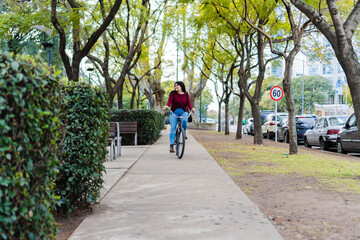 Obraz premium Young latin woman riding her bike on the sidewalk in a sunny day