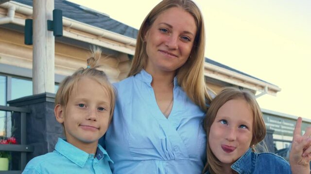 A beautiful mother and children are posing in front of the camera, the children are making faces and a fool. Mom with children is blond with blue eyes. Aryan race. Relationship in the family.