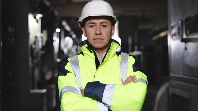 Portrait of confident engineer wearing safety vest and hard hat crossing arms at electrical control room. Confident pose of worker in safety uniform look to camera