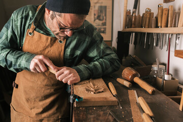 Side shot of a cabinetmaker working on a wood carving with a chisel.