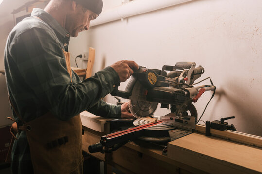 Side shot of a cabinetmaker cutting a wood strip with a circular saw.