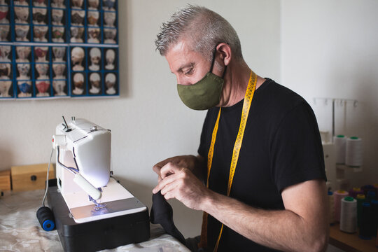 a mask-wearing tailor at work with his sewing machine