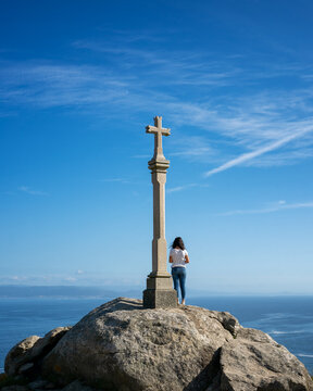 Woman on top a viewpoint rock with a cross sculpture in Finisterre