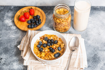 A bowl of cereal with blueberries with a wooden plate of strawberries and blueberries, a jar of cereal and a glass of fresh milk. A perfect breakfast to start your morning right.