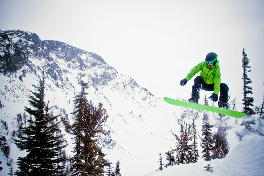 Snowboarder wearing green in mid-air after launching off snow jump.