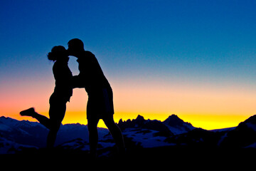 silhouetted Loving couple embrace and kiss on a mountain summit.