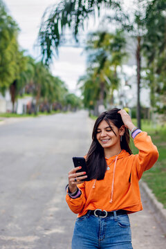 Happy hispanic teen girl looking at smart phone