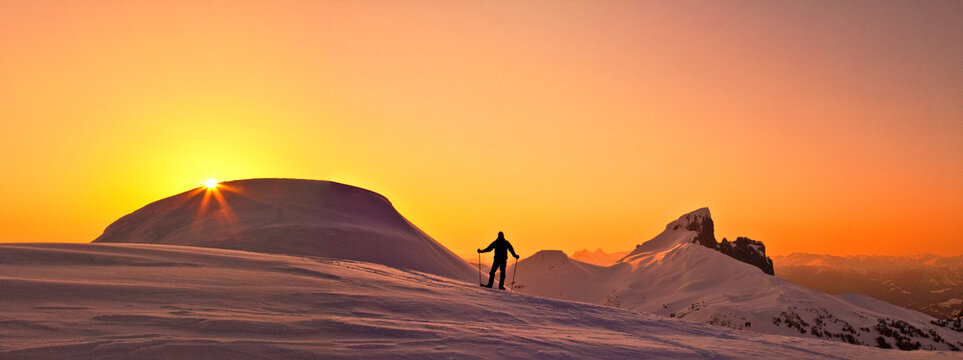 Panoramic view of explorer on snowy mountain ridge at sunset.