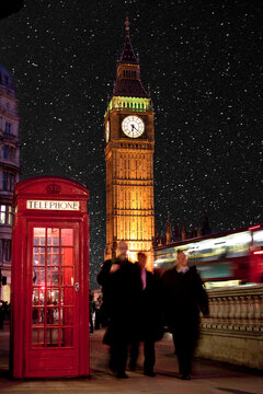Men in suits walk below Big Ben next to telephone booth and red bus.