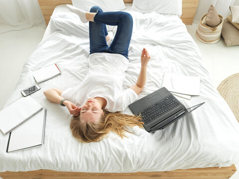 young blond female listening to the music onwhite bed with laptop