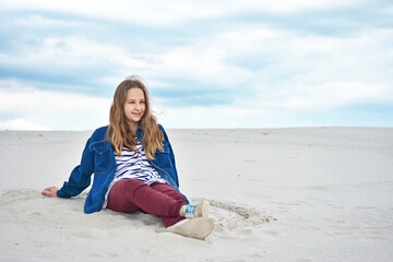 Teenage girl sitting on the sand and looking into the distance