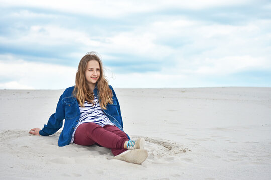 Teenage Girl Sitting On The Sand And Looking Into The Distance