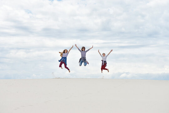 Girls with mom are jumping against the background of the sky and sand
